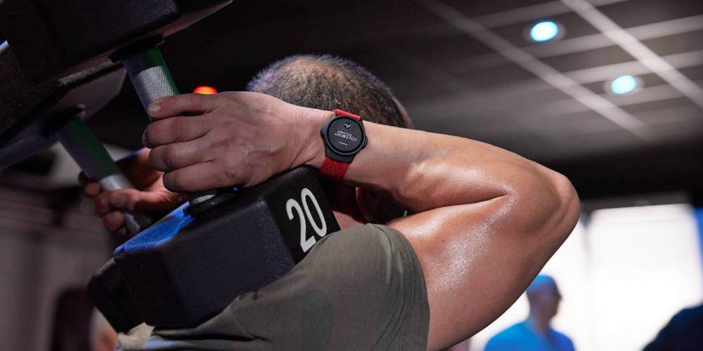 A man working out using dumbbells, wearing a Myzone heart rate monitor in the gym